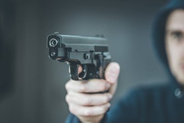 Soyguncu ya da suçlu siyah bir silahla nişan alıyor, yüzü bulanık.