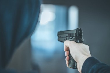 Soyguncu ya da suçlu siyah bir silahla nişan alıyor, yüzü bulanık.