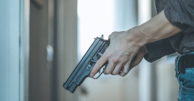 Gizli polis memuru elinde siyah bir silah tutuyor, vurmaya hazır.