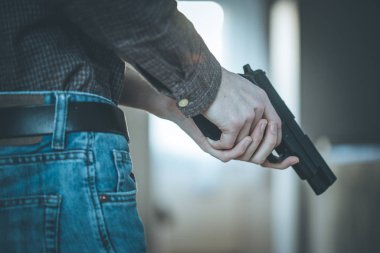 Gizli polis memuru elinde siyah bir silah tutuyor, vurmaya hazır.