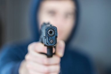 Soyguncu ya da suçlu siyah bir silahla nişan alıyor, yüzü bulanık.