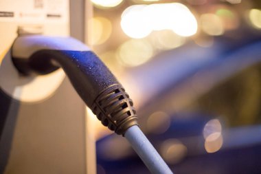 Elektrikli araba şarj kablosuyla şarj oluyor ve şarj noktasına gidiyor. Gece.