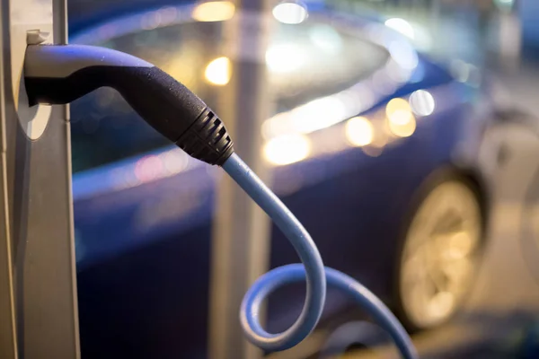 Elektrikli araba şarj kablosuyla şarj oluyor ve şarj noktasına gidiyor. Gece.