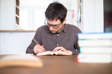 Erkek öğrenci evde araştırma yapıyor ve öğreniyor, kitap yığını bulanık