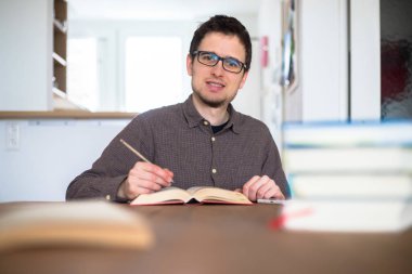 Erkek mutlu öğrenci evde araştırma ve öğrenme, kitap yığını bulanık