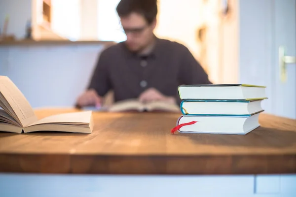 Male student researching and learning at home. Stack of books, person in blurry background.