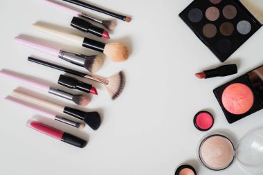 Makyaj fırçaları ve diğer aksesuarlar. Ruj, rimel, oje, göz farı, pudra, kirpik ve fondöten. Makyaj ürünleri beyaz arka planda, üst görünümde. 