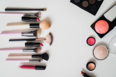 Makyaj fırçaları ve diğer aksesuarlar. Ruj, rimel, oje, göz farı, pudra, kirpik ve fondöten. Makyaj ürünleri beyaz arka planda, üst görünümde. 