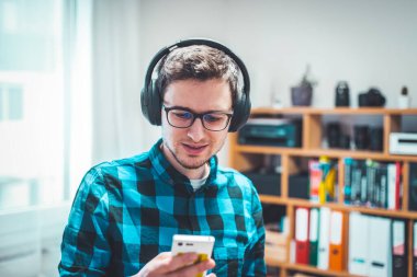 Mavi gömlekli genç beyaz adam kablosuz kulaklıkla müzik dinliyor.