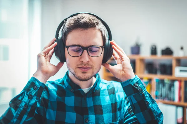 Young Caucasian man with checked blue shirt is listing to music with wireless headphones