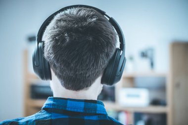 Mavi gömlekli genç beyaz adam kablosuz kulaklıkla müzik dinliyor. Başının arkasına..