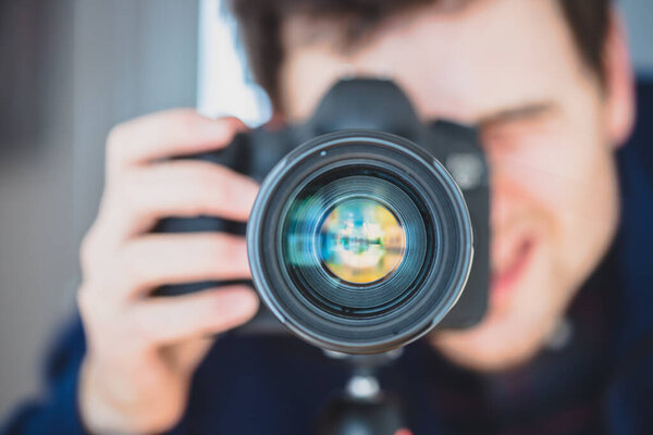 Фотограф стоит за профессиональной камерой с телеобъективом на штативе
