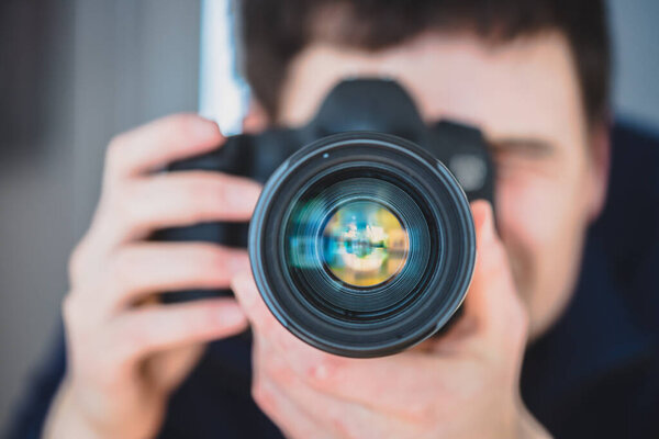 Фотограф стоит за профессиональной камерой с телеобъективом на штативе
