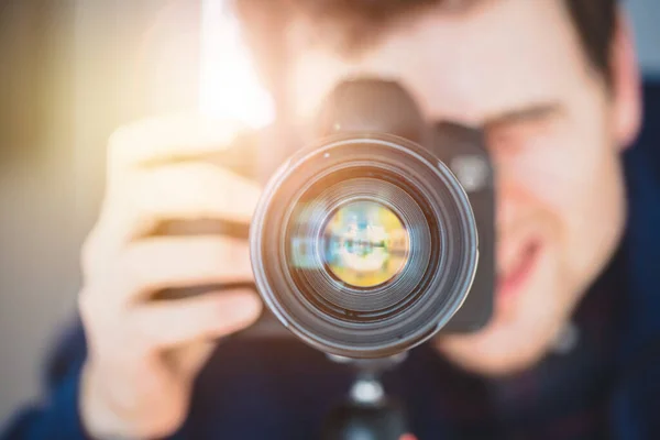 Fotoğrafçı, tripodunda telefoto lensleriyle profesyonel bir kameranın arkasında duruyor. Güneş ışığı.