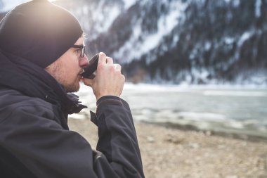 Beyaz bir adam elinde bir fincan çay tutuyor, kış vakti.