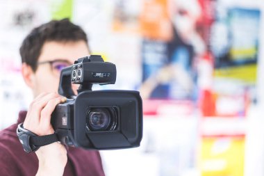 Erkek kameramanın elinde profesyonel bir kamera var. Geçmişi bulanık.