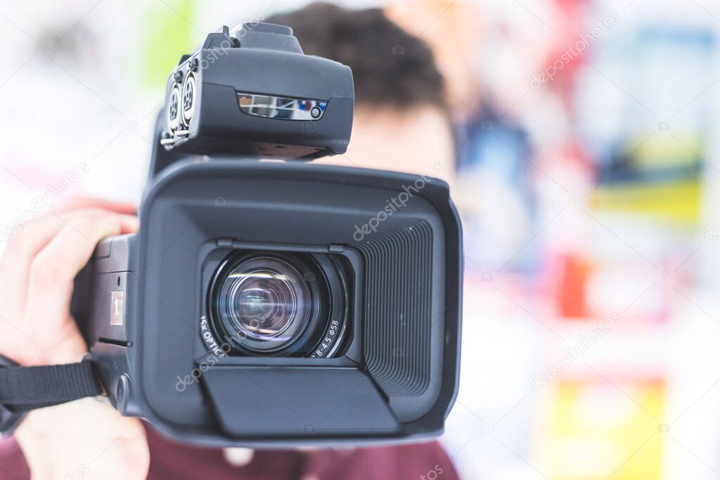 Male cameraman is holding a professional video camcorder, blurry background