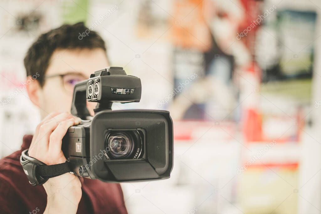 Male cameraman is holding a professional video camcorder, blurry background