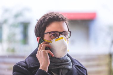 Dışarıda solunum maskesi ve akıllı telefonu olan genç bir iş adamı. Flue ve corona mevsimi. 