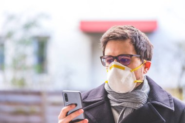 Dışarıda solunum maskesi ve akıllı telefonu olan genç bir iş adamı. Flue ve corona mevsimi. 