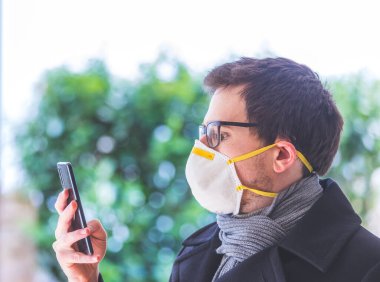 Dışarıda solunum maskesi ve akıllı telefonu olan genç bir iş adamı. Flue ve corona mevsimi. 