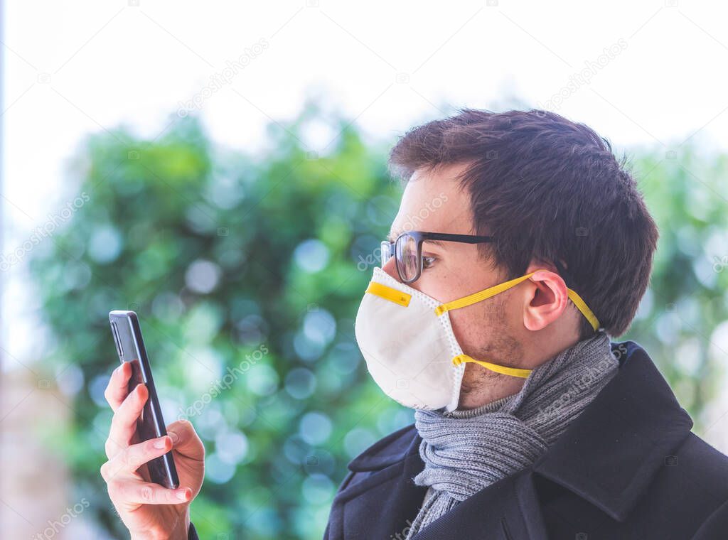 Young business man outdoors with a breathing mask and smartphone. Flue and corona season. 
