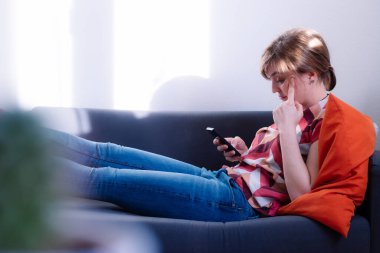 Sarışın, çekici kız kanepede uzanıyor ve erkek arkadaşıyla mesajlaşıyor.