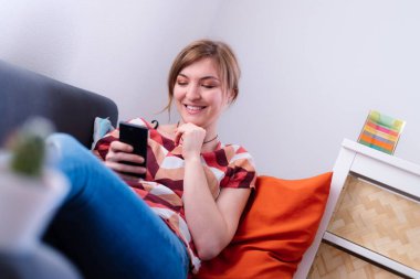 Sarışın, çekici kız kanepede uzanıyor ve erkek arkadaşıyla mesajlaşıyor.