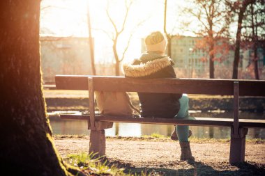 Parktaki bankta güneşlenmekten hoşlanan genç bir kadının arka görüntüsü.