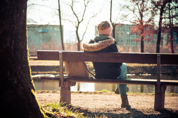 Back view of young woman who is enjoying the sun on a park bench, spring time