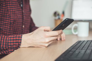 Genç adam cep telefonunu elinde tutuyor, ev ofisinin içinde.