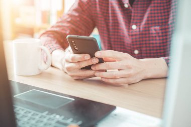 Genç adam cep telefonunu elinde tutuyor, ev ofisinin içinde.