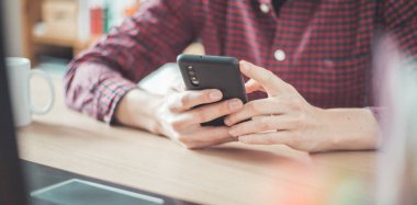 Genç adam cep telefonunu elinde tutuyor, ev ofisinin içinde.