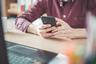 Genç adam cep telefonunu elinde tutuyor, ev ofisinin içinde.