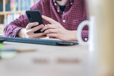 Genç adam cep telefonunu elinde tutuyor, ev ofisinin içinde.