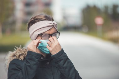 Dışarıda maskeli, gözlüklü, lekeli gözlüklü genç bir kadın. 