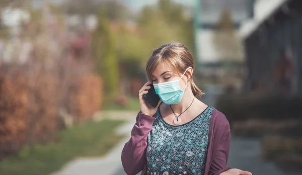 屋外でフェイスマスクとスマートフォンを身に着けている若い女性 コロナウイルスとインフルエンザの季節 — ストック写真