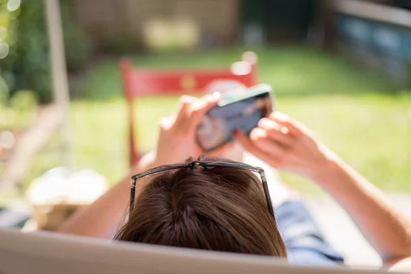 Girl is sitting on the sunny porch, enjoying the day and using her smartphone