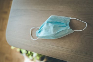 Yüz maskesi ya da cerrahi maske tahta bir masanın üzerinde duruyor, günlük rutin.