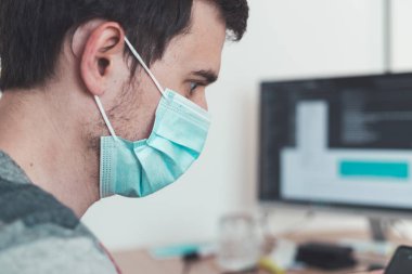 Corona krizi sırasında yüz maskesi takan genç adam ofiste çalışıyor..