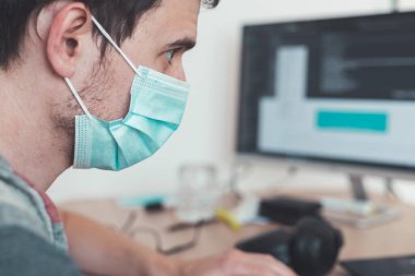 Corona krizi sırasında yüz maskesi takan genç adam ofiste çalışıyor..