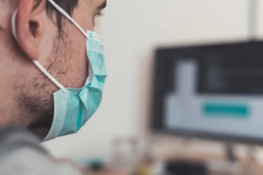 Corona krizi sırasında yüz maskesi takan genç adam ofiste çalışıyor..