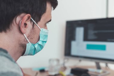 Corona krizi sırasında yüz maskesi takan genç adam ofiste çalışıyor..