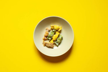 Krema kâsesinde servis edilen karamel şekilli doldurulmuş makarna sarı arka plan manzaralı.