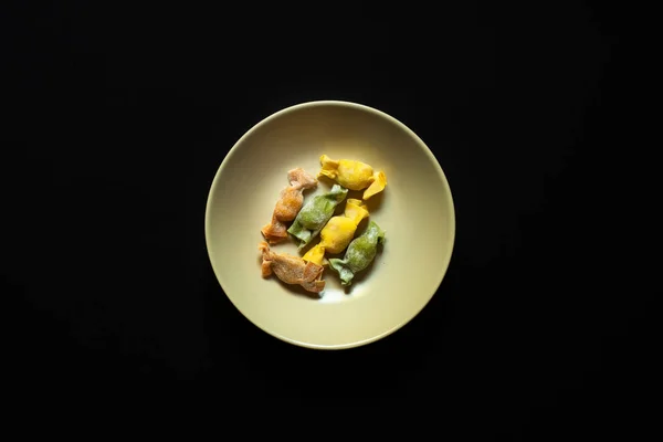 Nadívané těstoviny s caramelle tvar sloužil v černé míse přes černé pozadí horní pohled — Stock fotografie