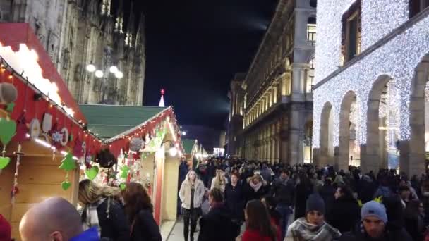 人々はミラノのドゥオーモの隣にあるコルソ ヴィットリオ エマヌエーレの伝統的なクリスマスマーケットを訪れます — ストック動画