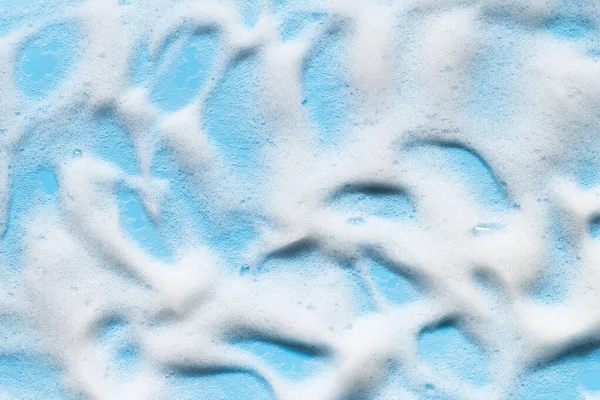 Soap foam on blue surface. Shampoo, cleanser, shower gel bubbles.  Bath hygiene background. Abstract cleansing foam splashes