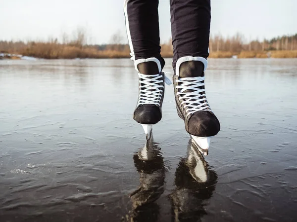 Piernas de una chica en patines de hockey negro en el hielo de un primer plano del lago. En el fondo un bosque — Foto de Stock