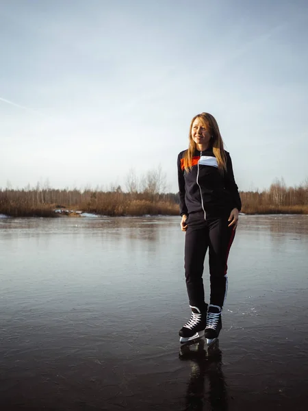 En ung vacker flicka åker skridskor på isen i en sjö. I bakgrunden en skog — Stockfoto