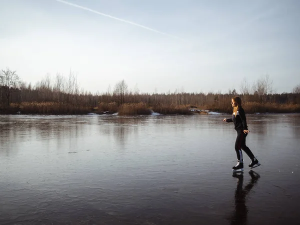 En ung flicka i en träningsoverall skridskor på en frusen sjö — Stockfoto